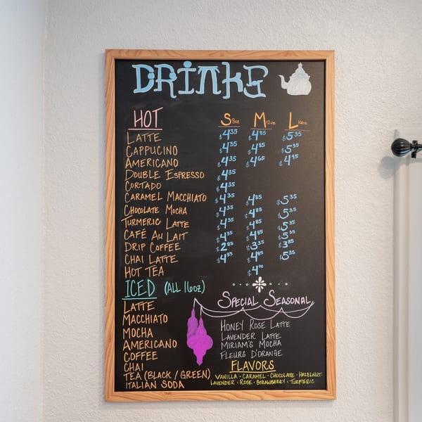 A Cafe Miriam chalkboard menu displays hot and iced drinks, seasonal specials, and flavor options.