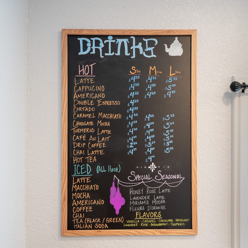 A Cafe Miriam chalkboard menu displays hot and iced drinks, seasonal specials, and flavor options.