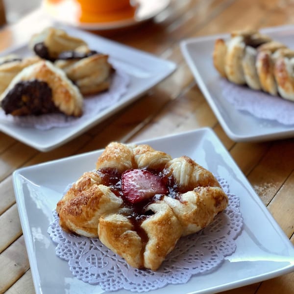 A strawberry danish with two other pastries on white plates on a wooden table.