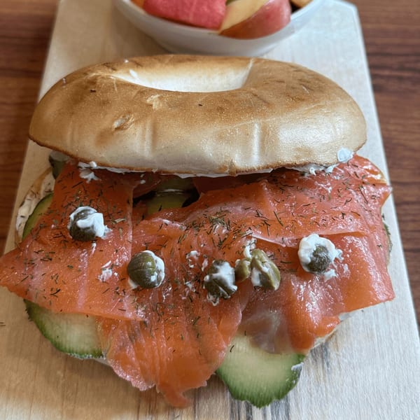 A Cafe Miriam bagel with smoked salmon, cream cheese, capers, and avocado on a wooden board.