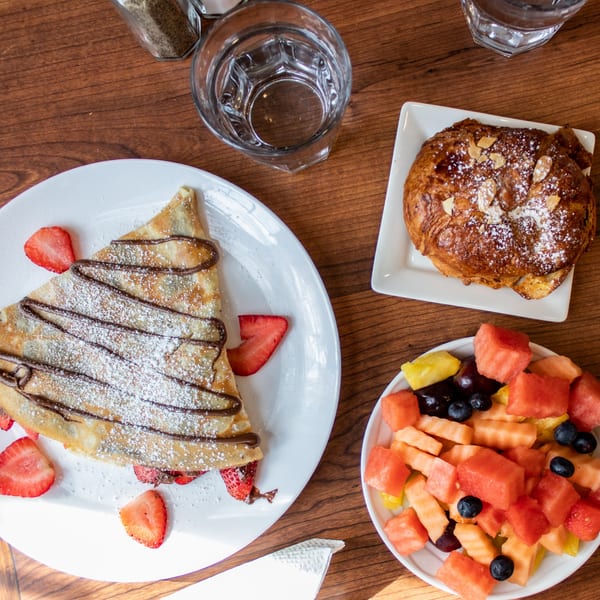 Overhead view of a breakfast spread with a chocolate strawberry crepe, croissant, and fruit salad.