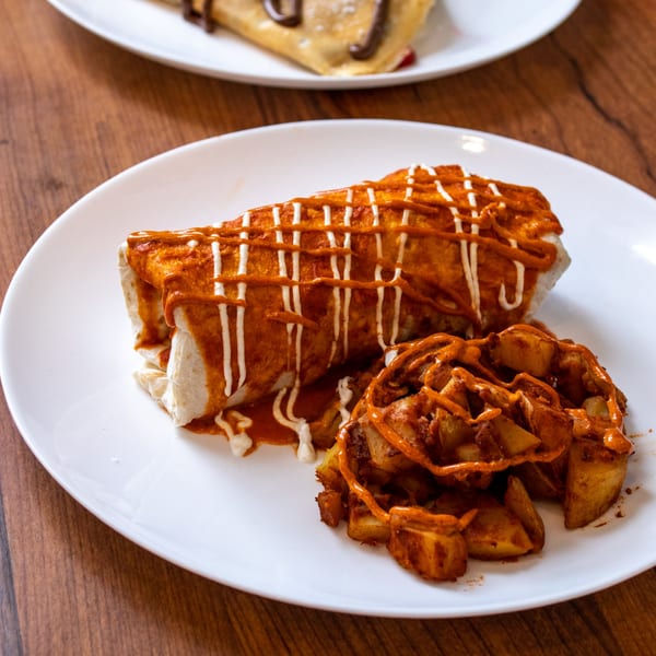 Cafe Miriam's breakfast burrito, drizzled with red and white sauce, served with seasoned potato wedges.