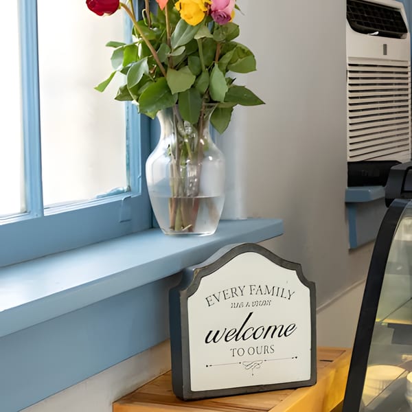A vase of colorful roses on a blue window sill next to a "Welcome to Ours" sign.