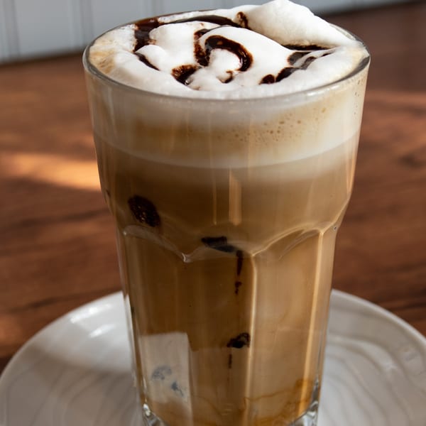 Iced coffee with whipped cream and chocolate drizzle in a tall glass on a white saucer.