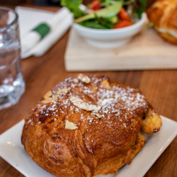 Almond croissant with powdered sugar and sliced almonds, with a side salad in the background.