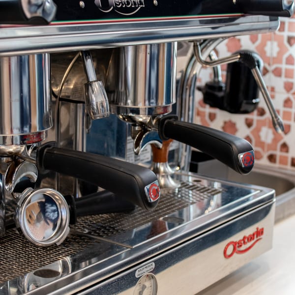 Close-up of a shiny chrome espresso machine with two portafilters and a pressure gauge.