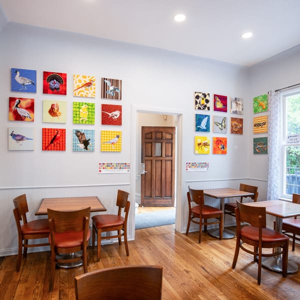 Cafe Miriam's dining room with wooden tables and chairs, adorned with colorful bird and insect artwork.