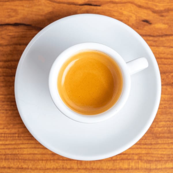 Overhead view of a white cup of espresso with rich crema on a wooden table.