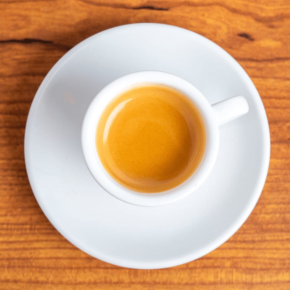 Overhead view of a white cup of espresso with rich crema on a wooden table.