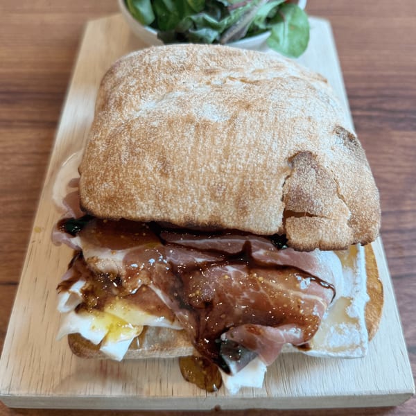 Cafe Miriam's breakfast sandwich with prosciutto, cheese, and fig jam on ciabatta, served with a side salad.
