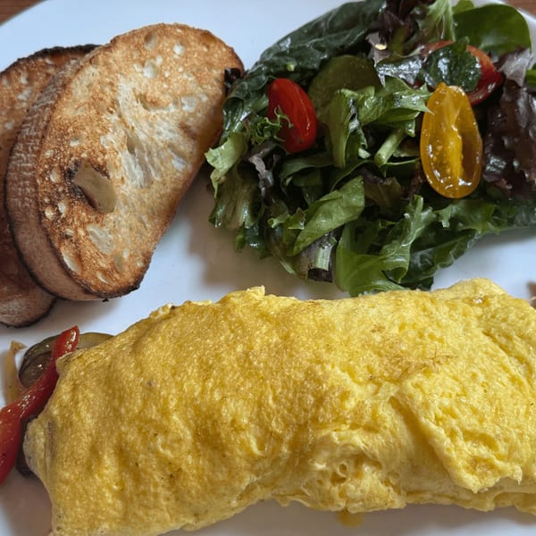Cafe Miriam's breakfast omelet with toast and a side salad on a white plate.