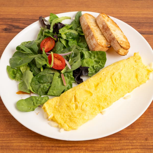Cafe Miriam's breakfast omelet with a side salad, cherry tomatoes, and toasted baguette slices.